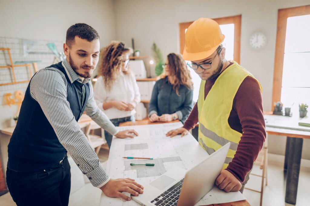 Professionals in hard hats reviewing blueprints around a table – construction consulting firm