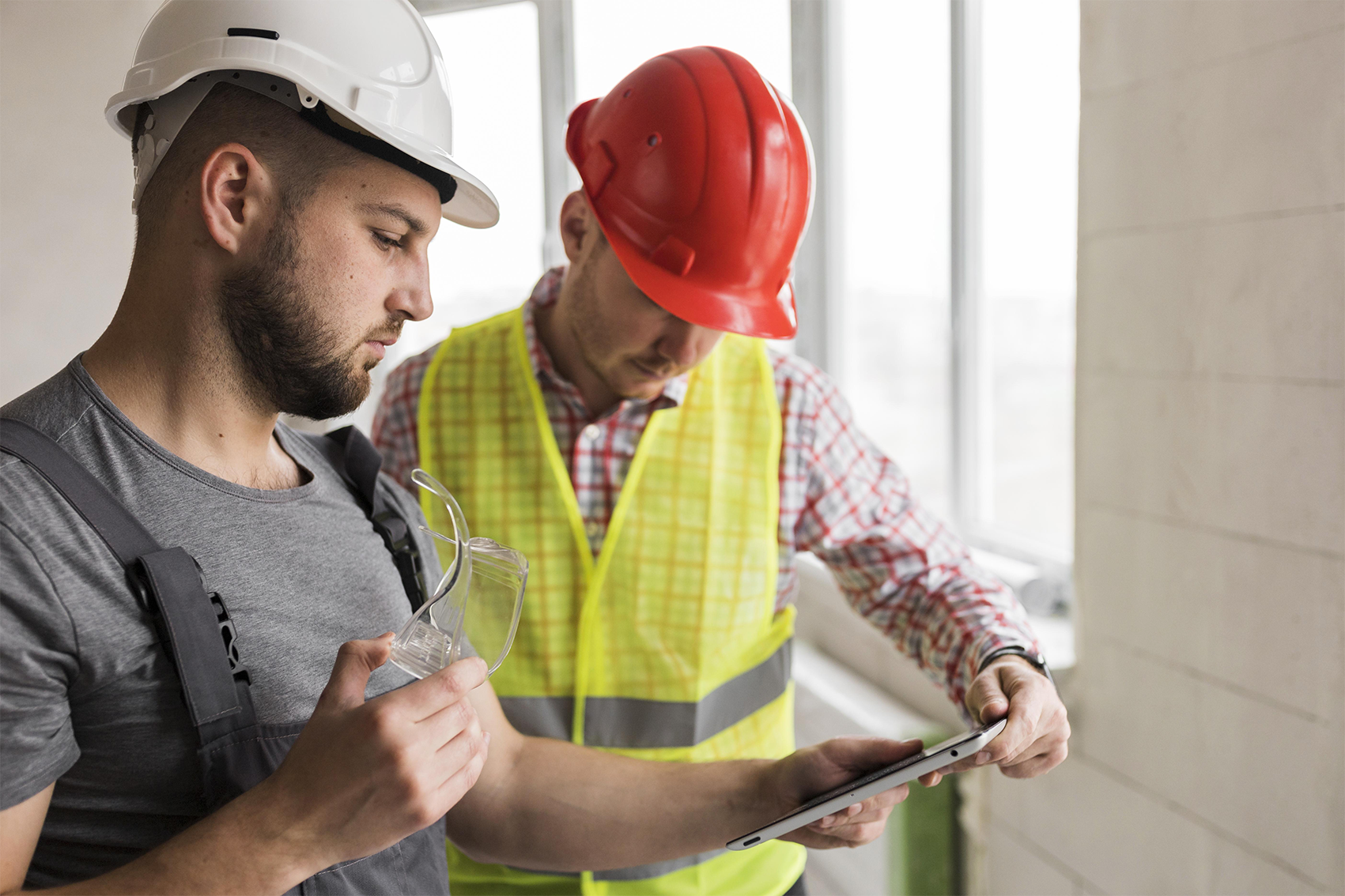 Senior living construction site risk management with two professionals in safety gear reviewing project details on a tablet, assessing progress and safety compliance during ground-up development – zumBrunnen