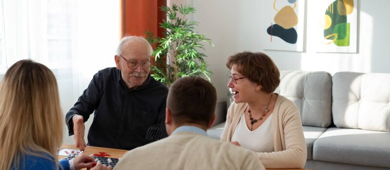 Older couple and younger couple sitting at a coffee table playing a game – zumBrunnen construction consulting