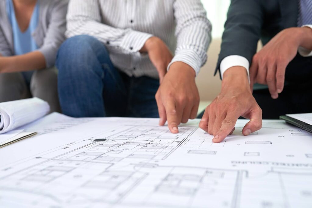 Three young professionals pointing to a blueprint map of a construction project.
