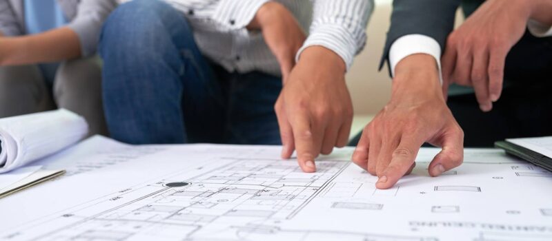 Three young professionals pointing to a blueprint map of a construction project – zumBrunnen construction consulting